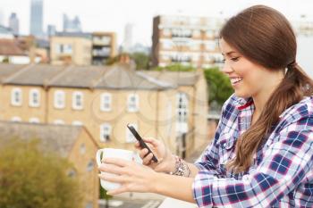 Woman Using Mobile Phone On Rooftop Garden Drinking Coffee