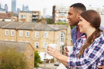 Couple Relaxing Outdoors On Rooftop Garden Drinking Coffee