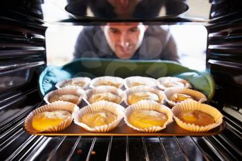 Man Putting Cupcakes Into Oven To Bake
