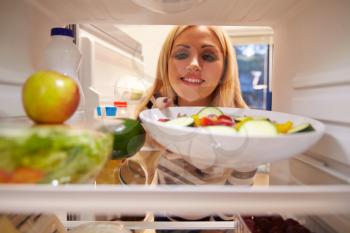 Woman Looking Inside Fridge Full Of Food And Choosing Salad