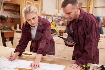 Carpenter With Apprentice Looking At Plans In Workshop