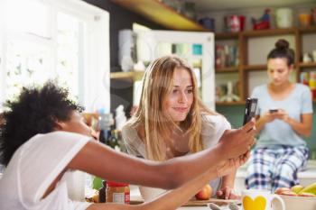 Female Friends Making Breakfast Whilst Checking Mobile Phone