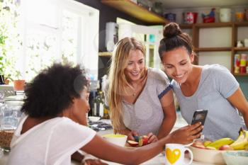 Female Friends Making Breakfast Whilst Checking Mobile Phone