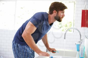 Man In Pajamas Brushing Teeth In Bathroom