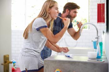 Couple In Pajamas Brushing Teeth In Bathroom