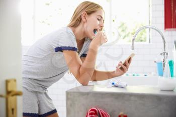 Woman In Pajamas Brushing Teeth And Using Mobile Phone