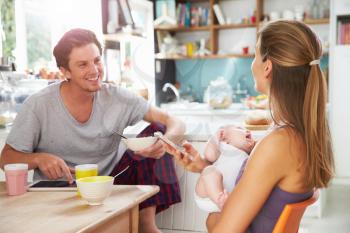 Family With Baby Girl Use Digital Devices At Breakfast Table