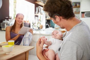 Family With Baby Girl Use Digital Tablet At Breakfast Table