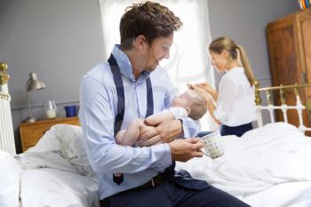Parents With Young Baby Dressing For Work In Bedroom