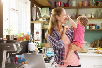 Mother With Young Daughter Using Laptop In Kitchen