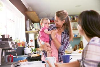 Mother With Young Daughter Talking To Friend In Kitchen