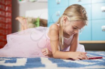Pretty Girl Lying On Floor Of Bedroom With Digital Tablet
