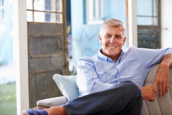 Portrait Of Smiling Mature Man Sitting On Sofa At Home