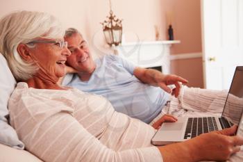 Senior Couple Lying In Bed Looking At Laptop Computer