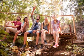 Group Of Friends On Walk Sitting On Wooden Bridge In Forest