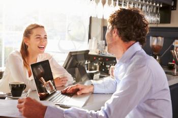 Male restaurant manager with laptop talking to waitress