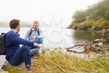 Father and young adult son talking by a lake