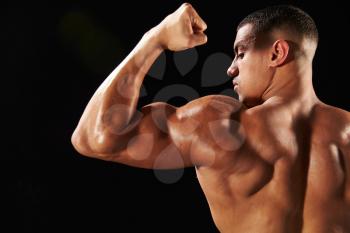 Male bodybuilder flexing bicep, back view with copy space