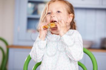 Young Girl Sitting At Table Eating Cookie