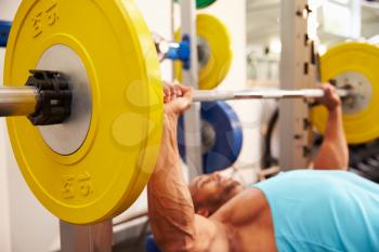 Young man bench pressing weights at a gym, side view