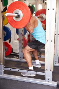 Man weightliftingbarbells at a squat rack in a gym