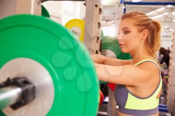 Woman leaning on a barbells at a squat rack in a gym