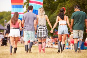 Friends walking together at a music festival site, back view