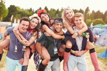 Friends giving piggy backs through music festival campsite