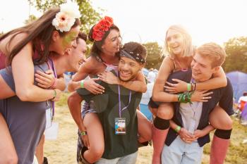 Friends giving piggy backs through music festival campsite