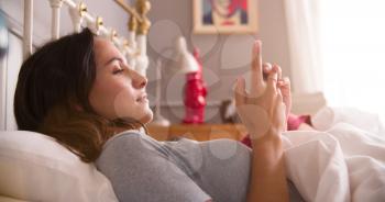 Woman Lying In Bed Checking Messages On Mobile Phone