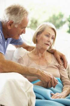 Husband Comforting Senior Woman Feeling Unwell Resting Under Blanket
