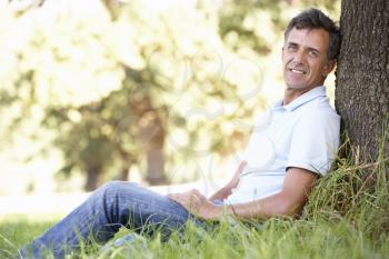 Middle Aged Man Relaxing In Countryside Leaning Against Tree