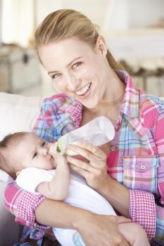 Young Mother With Baby Feeding On Sofa At Home