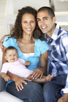 Young Family With Baby Relaxing On Sofa At Home