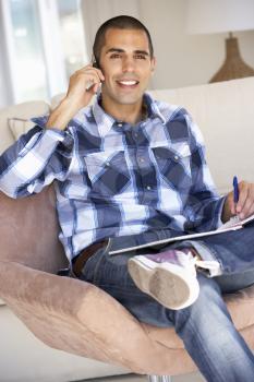 Young Man Doing Paperwork And Using Mobile Phone At Home