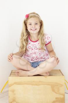 Young Girl Sitting On Wooden Toy Box Reading Book In Bedroom