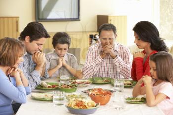 Extended Hispanic Family Saying Prayers Before Meal At Home