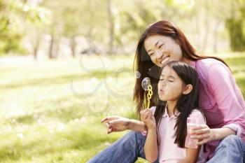 Asian mother and daughter blowing bubbles in park