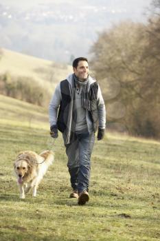 Man walking golden retriever in the country