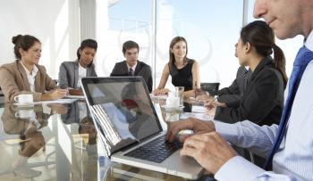 Close Up Of Businessman Using Laptop During Board Meeting Around Glass Table