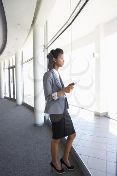Young Businesswoman Standing In Corridor Of Modern Office Building Using Tablet Computer