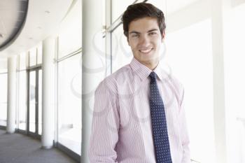 Portrait Of Young Businessman Standing In Corridor Of Modern Office Building