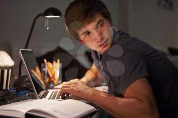 Guilty Looking Teenage Boy Studying At Desk In Bedroom In Evening On Laptop