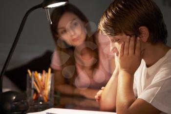 Teenage Sister Helping Stressed Younger Brother With Studies At Desk In Bedroom In Evening