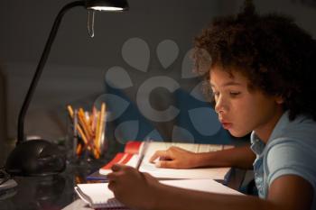 Young Boy Studying At Desk In Bedroom In Evening