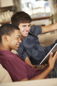 Two Teenage Boys Sitting On Sofa At Home Using Tablet Computer