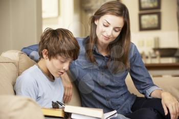 Mother Helping Son With Homework Sitting On Sofa At Home
