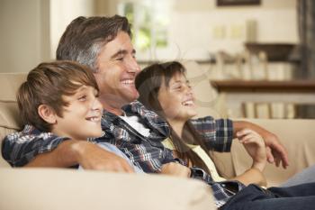 Father And Two Children Sitting On Sofa At Home Watching TV Together