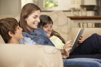 Mother And Two Children Sitting On Sofa At Home Using Tablet Computer