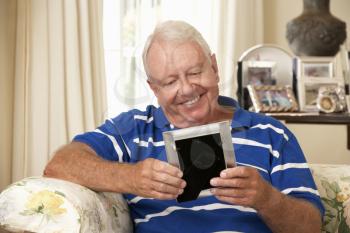 Happy Retired Senior Man Sitting On Sofa At Home Looking At Photograph